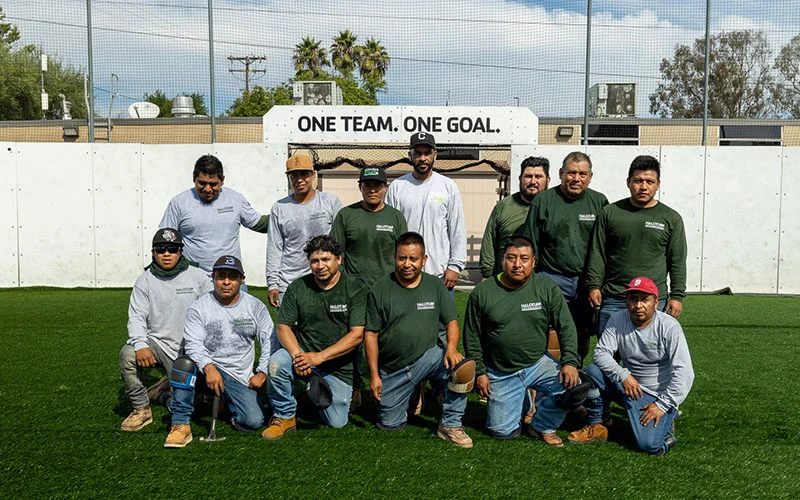 The HaloTurf install crew on a turf field under their One Team One Goal sign